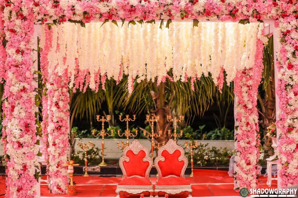 Open-air wedding stage with pink and white floral drapes and red chairs in soft evening light