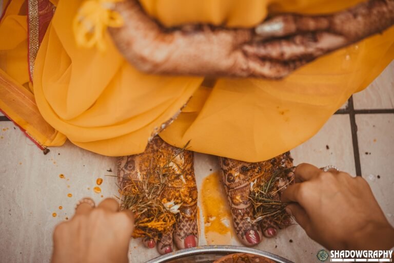 Haldi and turmeric being applied to a bride's mehndi-decorated feet during a wedding ceremony photographed by Shadowgraphy Studio