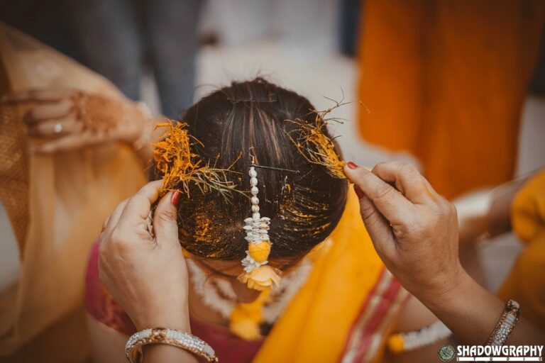 Family hands applying haldi to the bride hair during a morning haldi ceremony
