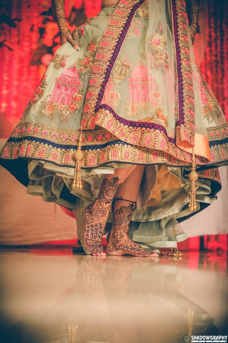 Bride's feet with intricate mehndi designs under an embroidered lehenga, photographed by Shadowgraphy Studio