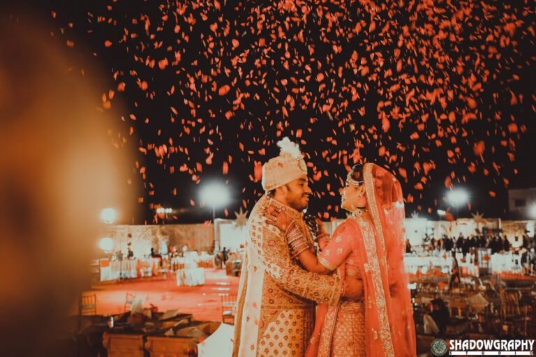 Bride and groom exchanging varmala garlands on stage under a shower of red rose petals