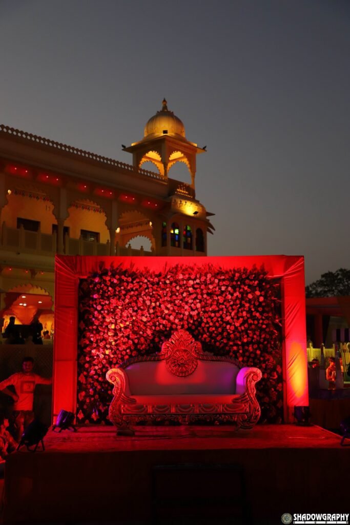 Outdoor evening wedding stage with a red floral backdrop in front of a lit heritage building