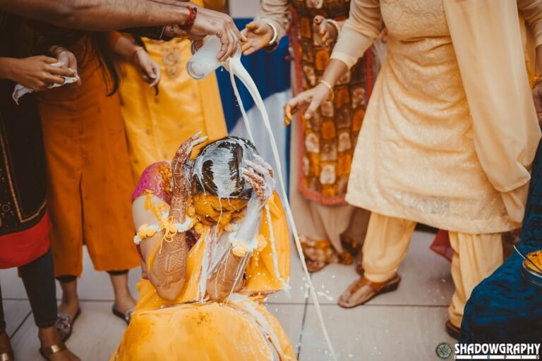 Family pouring milk over the bride during a haldi ritual in bright daylight