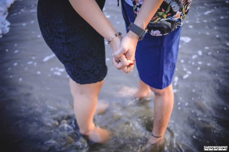 Couple holding hands while standing barefoot in the shallow water at a beach