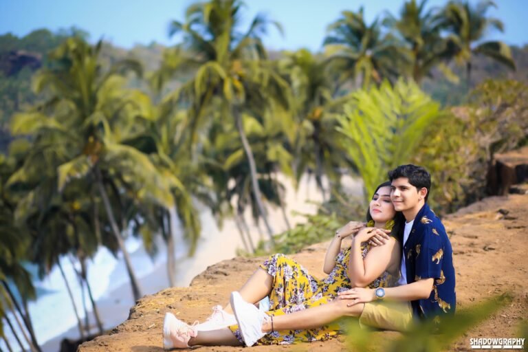 Couple sitting on a clifftop with palm grove and beach below during a pre-wedding shoot