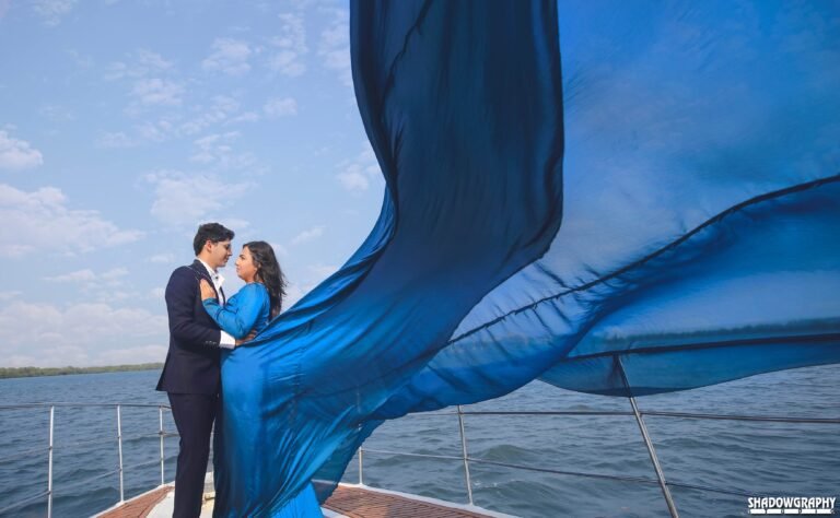 Couple embracing on a boat deck with a long blue gown flying in the breeze