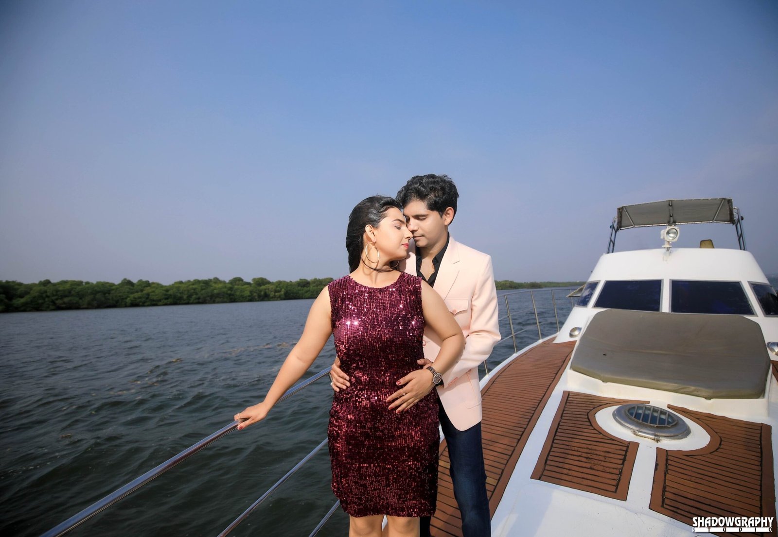 Couple standing close on the bow of a boat with open water and distant shoreline behind