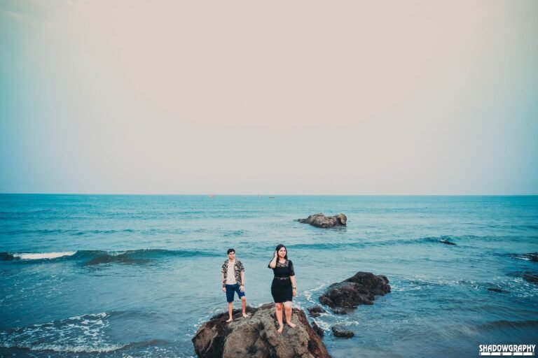 Aerial drone photo of a couple standing on rocks surrounded by the sea