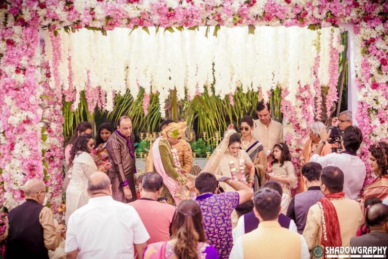Couple seated at the mandap under a floral canopy with family during the phera ceremony