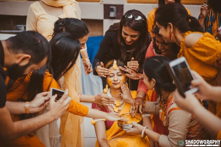 Friends and family applying haldi to the bride while photographing the moment on their phones