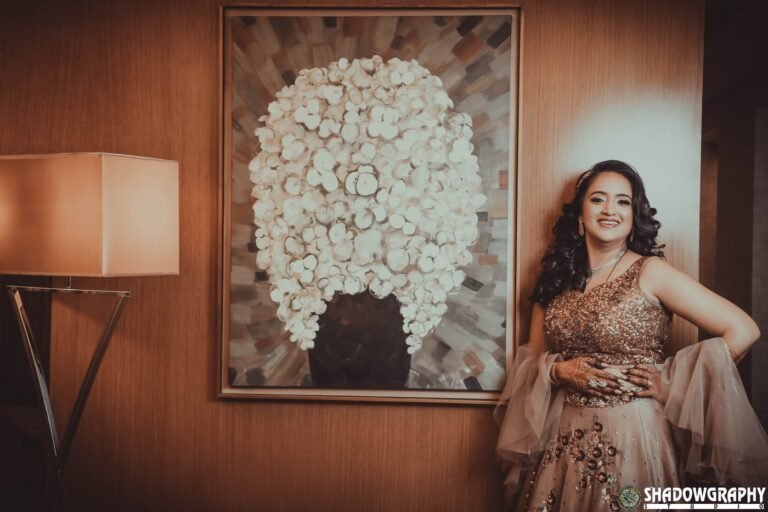 Bride in a gold reception gown posing by a white floral wall