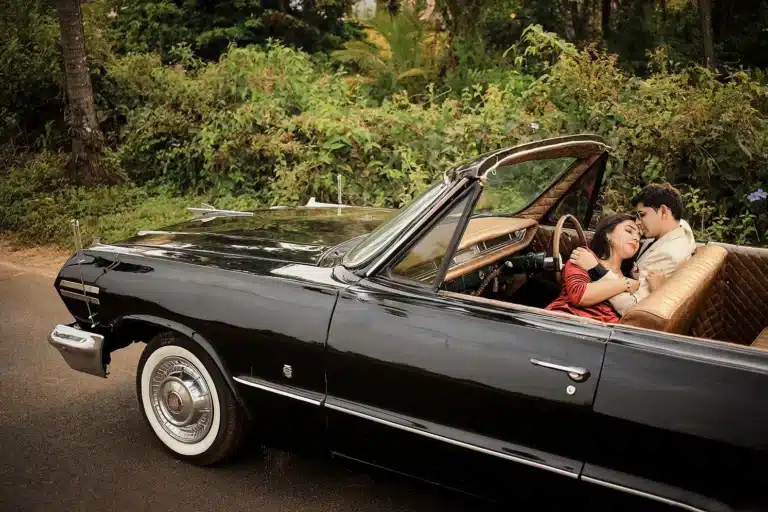 Couple sitting inside a black vintage convertible car on a tree-lined road