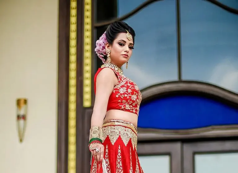 Bride in a red lehenga with detailed eye makeup, maang tikka and floral bridal hairstyle