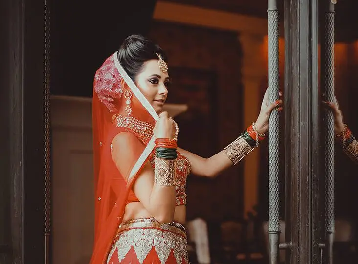 Bride at a doorway wearing layered bangles, necklace, earrings and maang tikka styled for a pre-wedding shoot