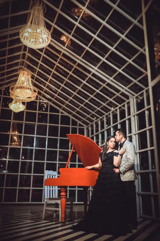 Couple beside a red piano in a glass house with chandeliers at Film City setup