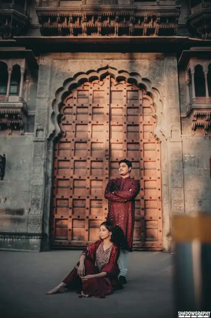 Couple in maroon outfits beside a carved door at Rajwada