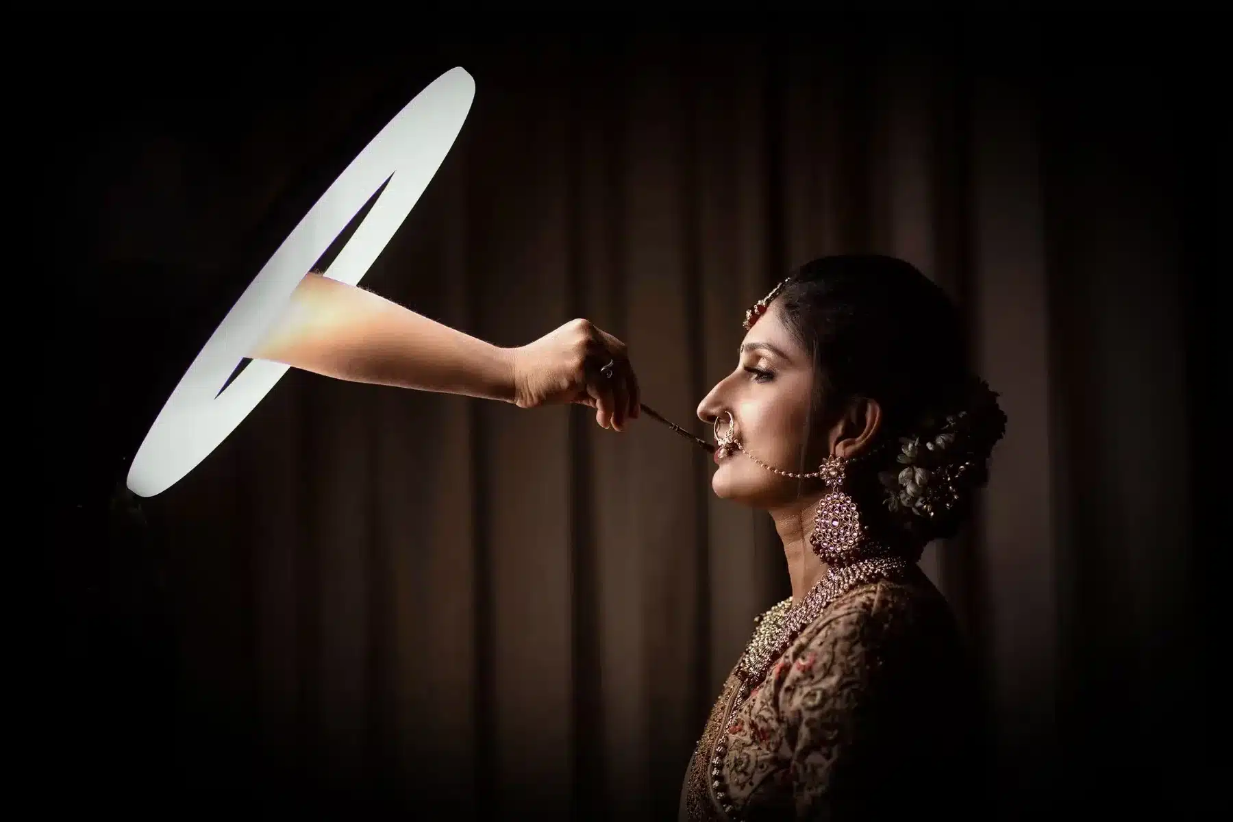 Candid bridal portrait of a bride in profile lit by a circular light on a dark backdrop
