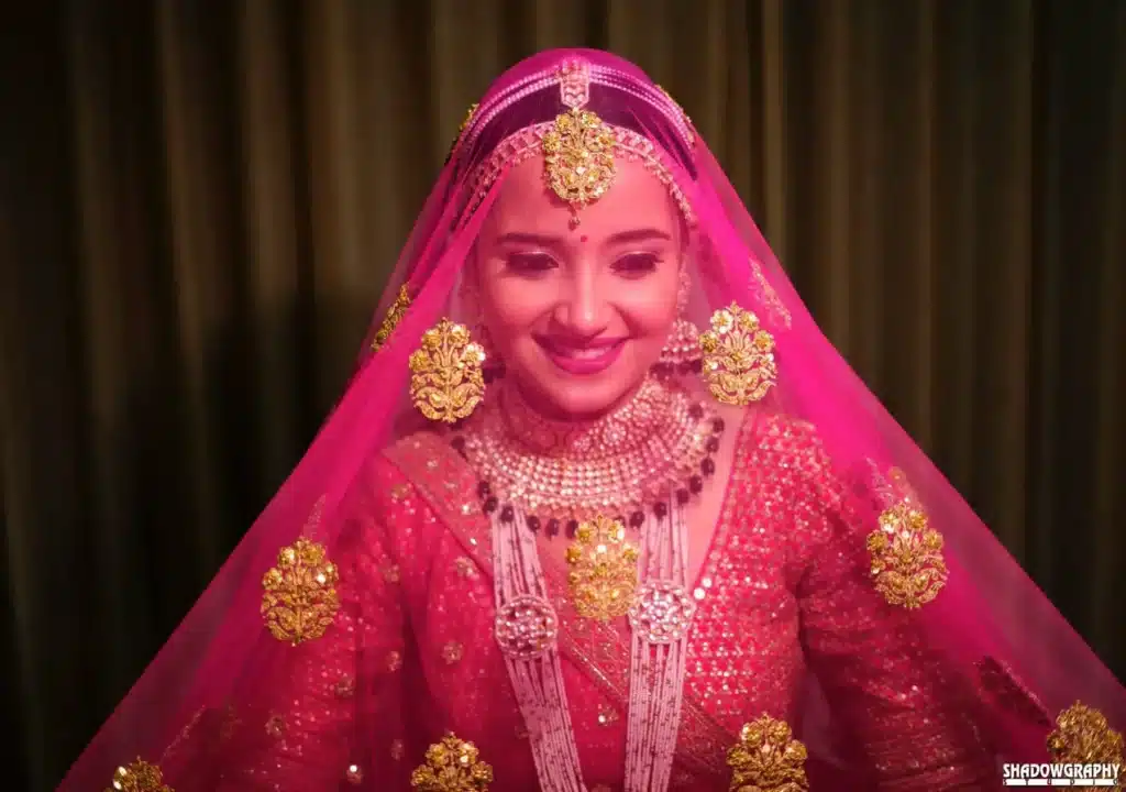 Smiling bride in a pink lehenga and heavy jewellery in a candid bridal portrait