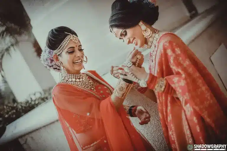 Two women in orange bridal outfits sharing a candid moment during bridal preparation