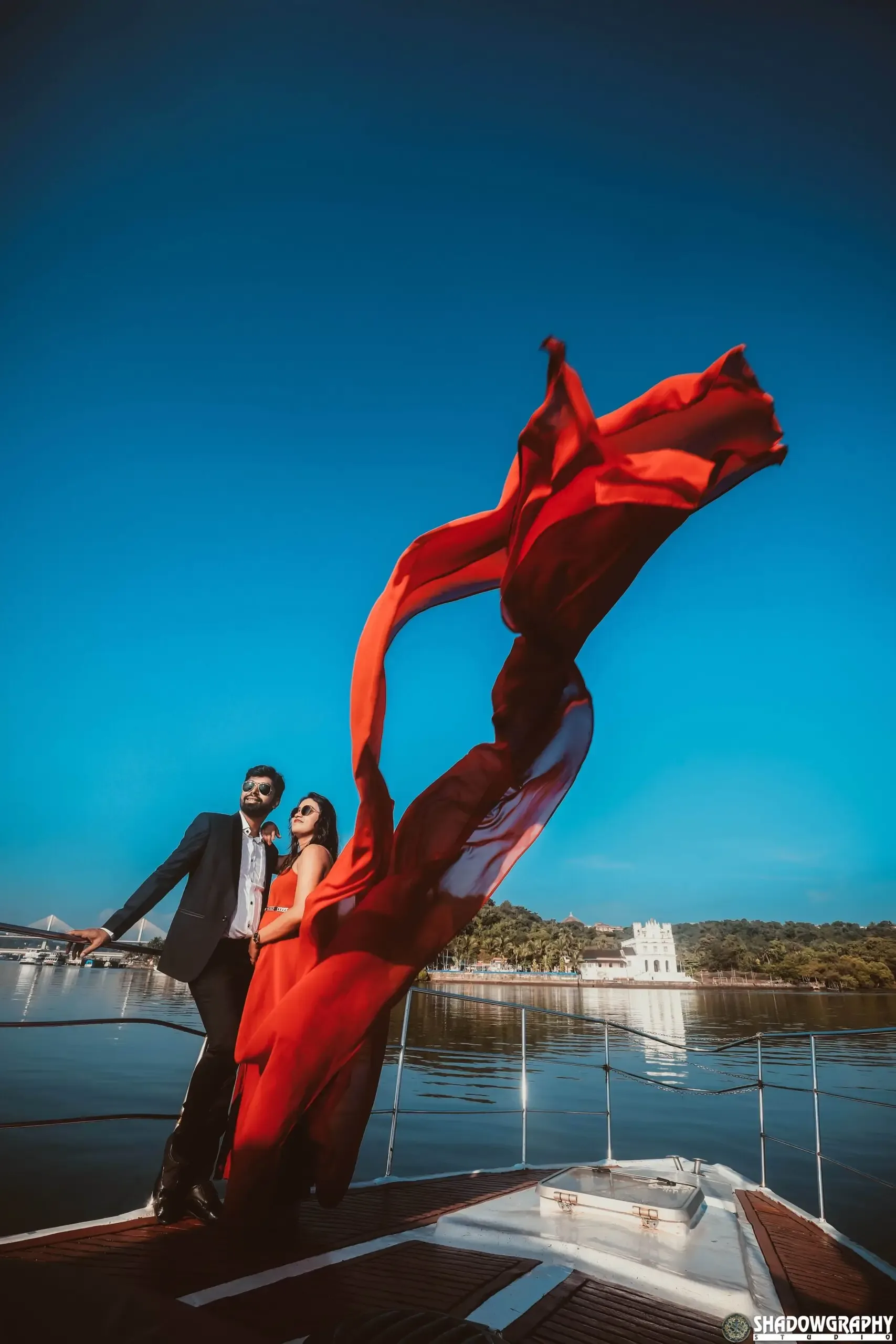 Pre-wedding couple on a boat with a long red fabric flying in the wind