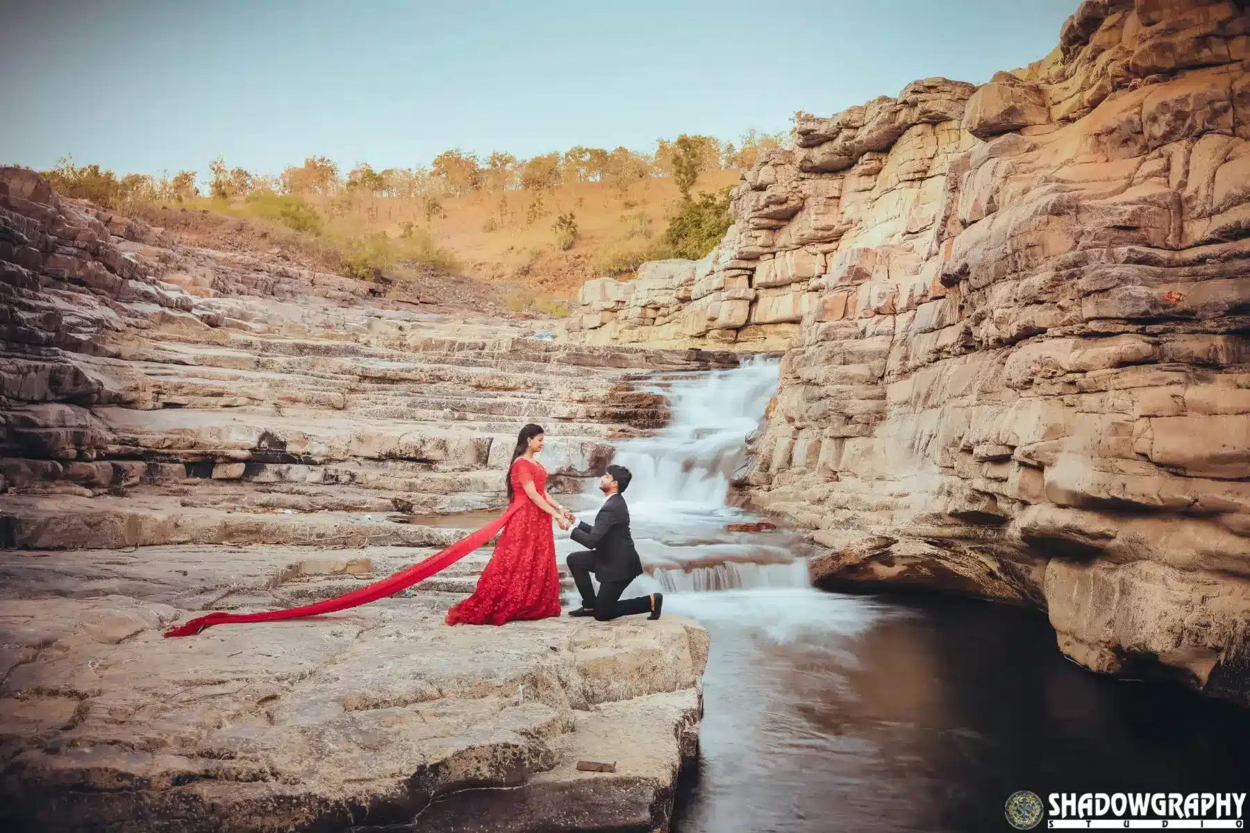 Couple in a red gown beside a rocky stream during a pre-wedding shoot